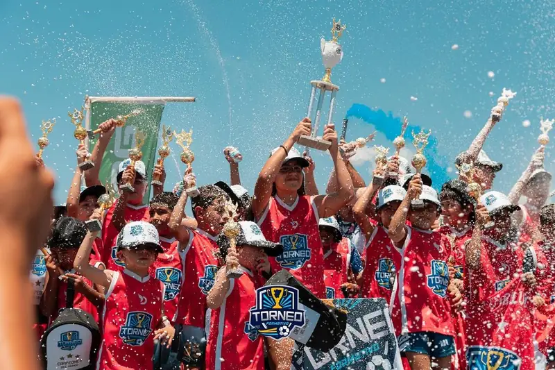 Chicos con camisetas rojas hechas por Daens levantando la copa del Torneo Formativo Tucumán